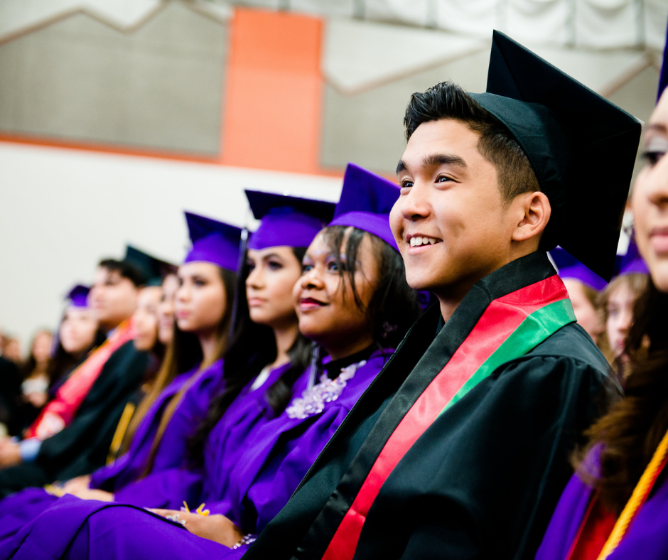 Smiling graduates seated in caps and gowns during a commencement ceremony