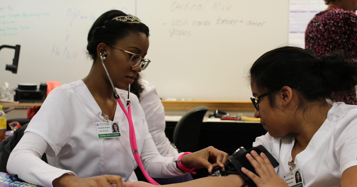 Two nurse aide students practicing taking blood pressure in a classroom setting