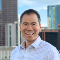 Professional headshot of Binh Diep smiling in front of a city skyline
