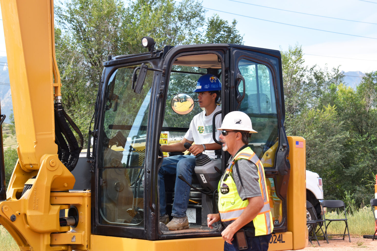 A high school student operates heavy machinery under the supervision of an instructor during hands-on construction training